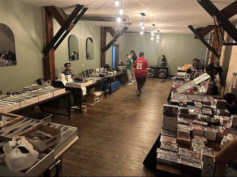 Tables of sports cards at the TrailSide memorabilia sale, with a guest in a red Taylor jersey.